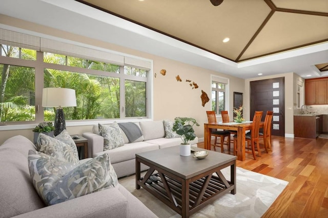 living room with crown molding, lofted ceiling, sink, and light wood-type flooring