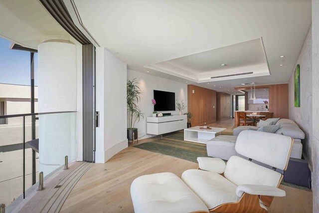 living room with floor to ceiling windows, light wood-type flooring, and a raised ceiling