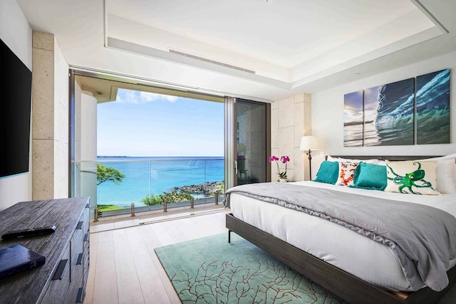 bedroom with a water view, a raised ceiling, access to outside, and light hardwood / wood-style floors