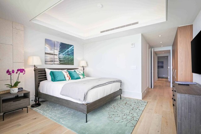 bedroom featuring a raised ceiling and light wood-type flooring