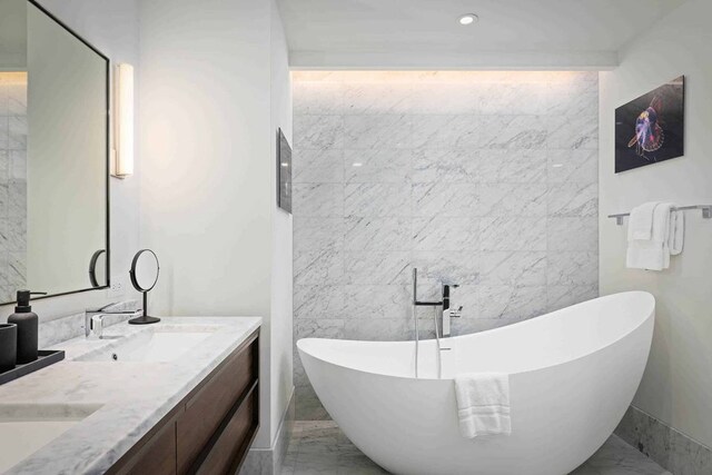 bathroom featuring dual sinks, tile flooring, vanity with extensive cabinet space, tile walls, and a bathing tub