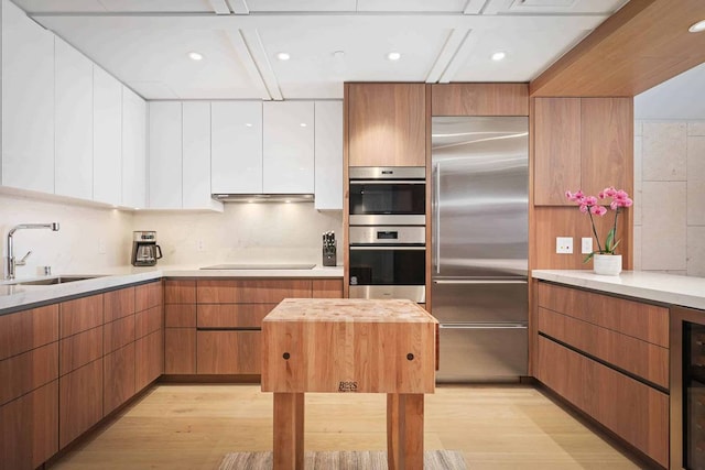 kitchen featuring stainless steel appliances, white cabinetry, butcher block counters, light wood-type flooring, and sink