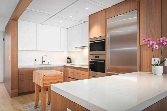 kitchen with appliances with stainless steel finishes, light hardwood / wood-style floors, sink, white cabinetry, and light stone countertops