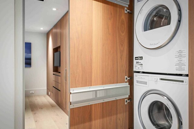 clothes washing area with light hardwood / wood-style flooring and stacked washer / dryer