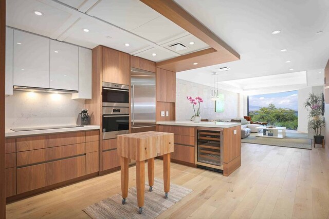 kitchen with stainless steel appliances, decorative light fixtures, wine cooler, light hardwood / wood-style flooring, and white cabinetry