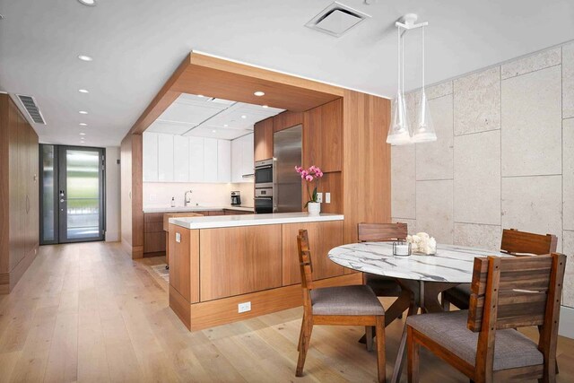 kitchen with kitchen peninsula, hanging light fixtures, light hardwood / wood-style floors, sink, and white cabinets