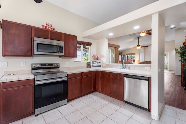 kitchen with light hardwood / wood-style flooring, stainless steel appliances, sink, ceiling fan, and vaulted ceiling