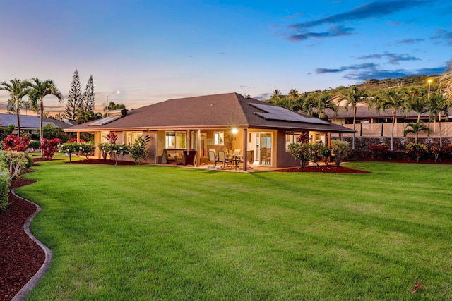 back house at dusk with a lawn, a patio area, and solar panels