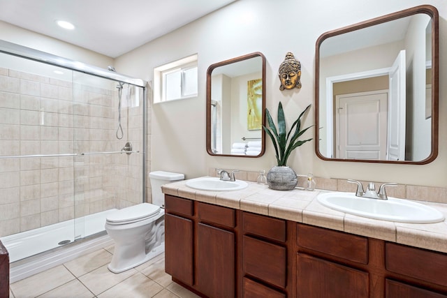 bathroom with double sink vanity, a shower with door, toilet, and tile patterned floors