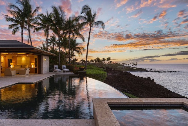 pool at dusk featuring a patio area, an outdoor hangout area, and a water view