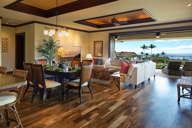 dining space featuring a tray ceiling, crown molding, ceiling fan with notable chandelier, and dark wood-type flooring