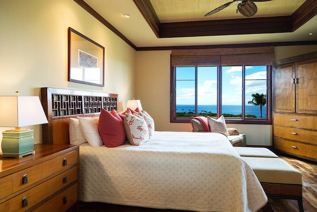 bedroom with ceiling fan, a raised ceiling, crown molding, wood-type flooring, and a water view