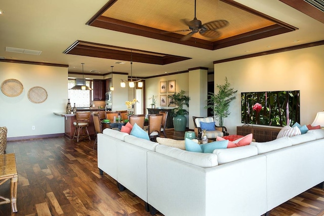 living room with a raised ceiling, dark wood-type flooring, crown molding, and ceiling fan