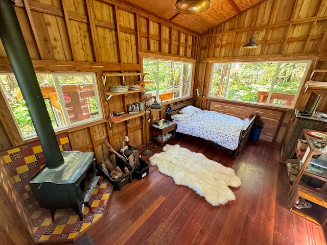 bedroom featuring hardwood / wood-style floors, wooden walls, a wood stove, and lofted ceiling