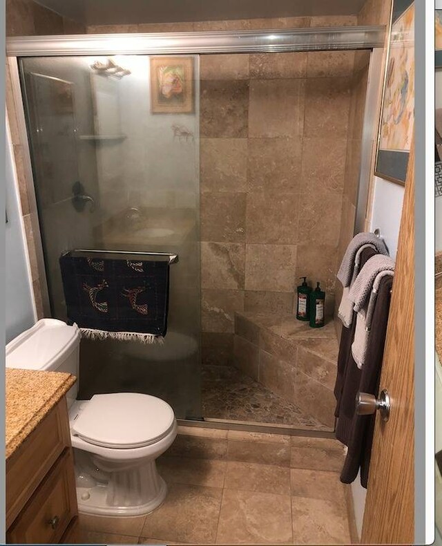 bathroom with tile floors, toilet, vanity, and an enclosed shower