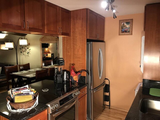 kitchen with dark stone counters, stainless steel appliances, ceiling fan, and light wood-type flooring