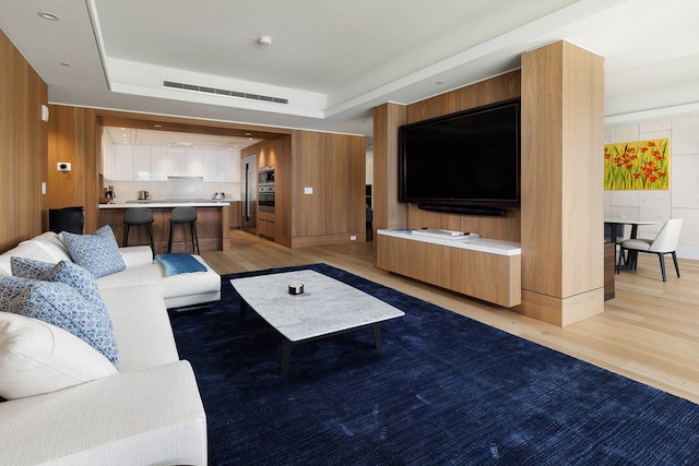 living room featuring wooden walls, a raised ceiling, and light hardwood / wood-style flooring