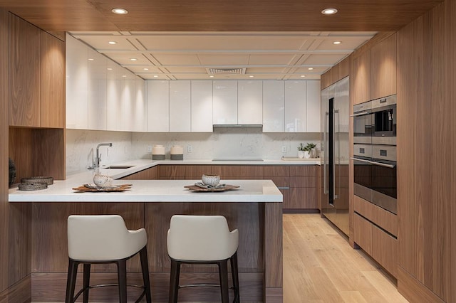 kitchen with a breakfast bar area, light hardwood / wood-style flooring, white cabinetry, and sink