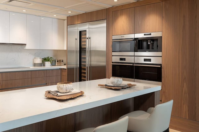 kitchen featuring white cabinets, backsplash, a kitchen breakfast bar, and appliances with stainless steel finishes