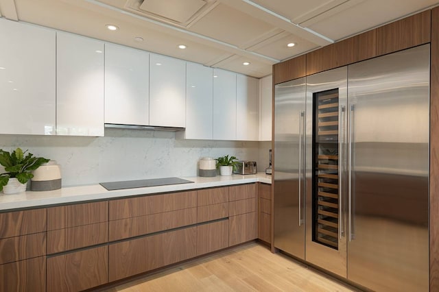 kitchen with stainless steel built in fridge, tasteful backsplash, light hardwood / wood-style flooring, white cabinetry, and black electric stovetop