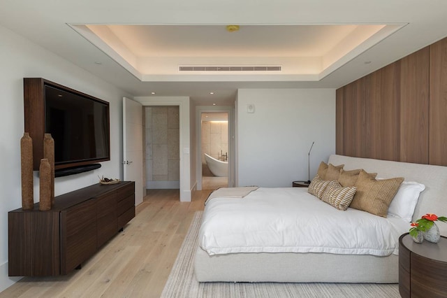 bedroom with connected bathroom, a tray ceiling, and light hardwood / wood-style floors