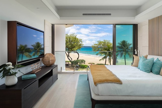 bedroom with a water view, a view of the beach, multiple windows, and light wood-type flooring