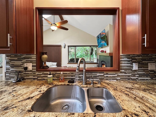 kitchen featuring sink, light stone counters, backsplash, and vaulted ceiling