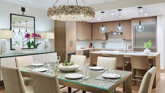 dining space with crown molding, wine cooler, sink, a chandelier, and light hardwood / wood-style flooring