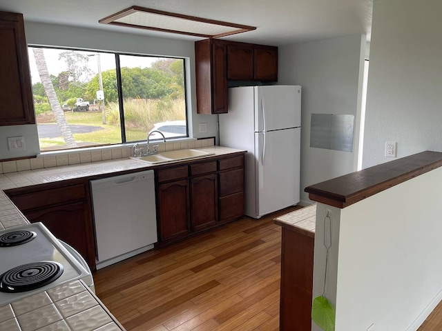 kitchen featuring light wood-type flooring, white appliances, tile countertops, sink, and dark brown cabinetry