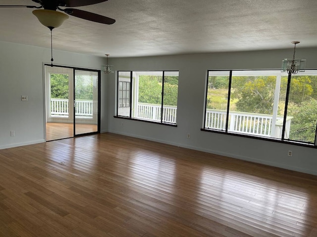 unfurnished room featuring dark hardwood / wood-style flooring, a textured ceiling, ceiling fan with notable chandelier, and plenty of natural light