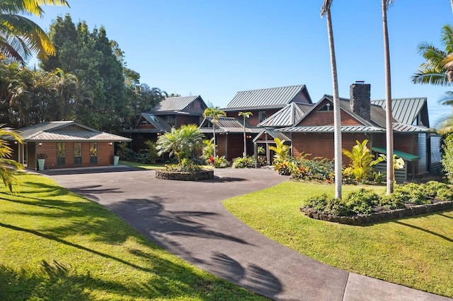 view of front facade with a chimney, a standing seam roof, metal roof, driveway, and a front lawn