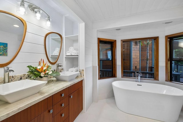 bathroom with double vanity, a freestanding tub, tile patterned flooring, and a sink