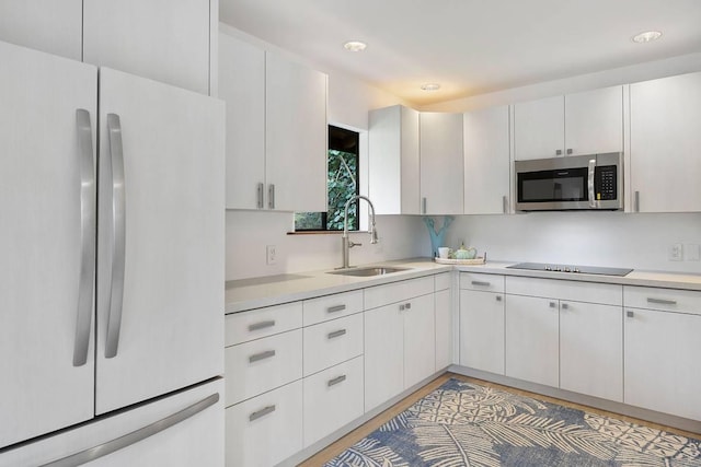 kitchen with light countertops, stainless steel microwave, freestanding refrigerator, a sink, and black electric cooktop