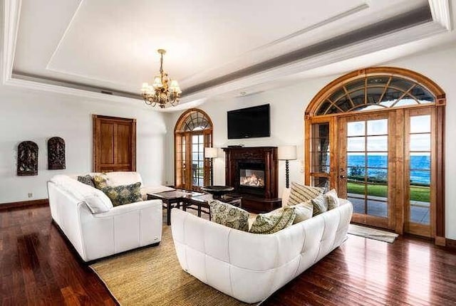 living room featuring a notable chandelier, a tray ceiling, dark wood-type flooring, and a wealth of natural light