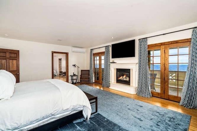 bedroom with french doors, wood-type flooring, a water view, access to outside, and a wall unit AC