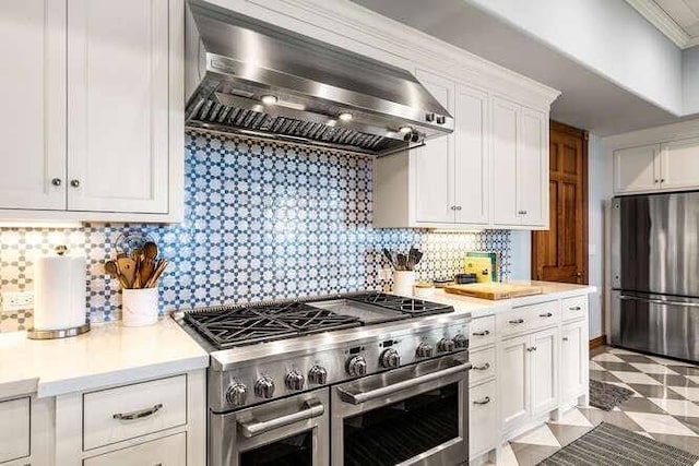 kitchen with tasteful backsplash, white cabinetry, light tile floors, stainless steel appliances, and wall chimney range hood