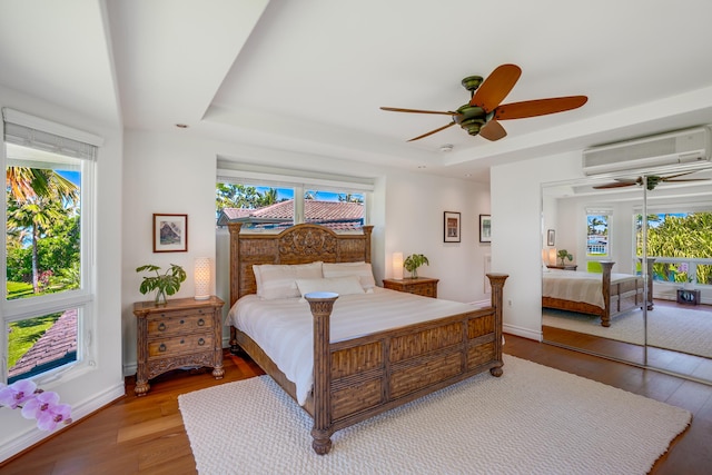 bedroom featuring ceiling fan, wood-type flooring, multiple windows, and a wall mounted AC