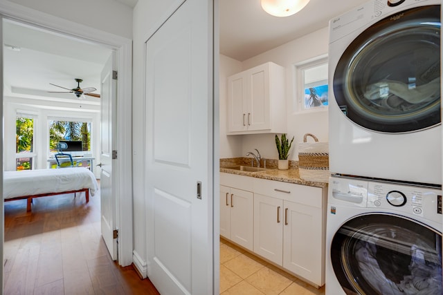 laundry area featuring cabinets, stacked washer and clothes dryer, sink, light hardwood / wood-style flooring, and ceiling fan