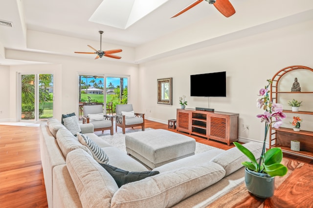 living room with a skylight, ceiling fan, and light hardwood / wood-style flooring