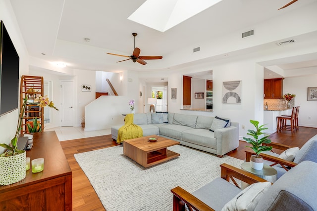 living room with a skylight, light hardwood / wood-style floors, and ceiling fan