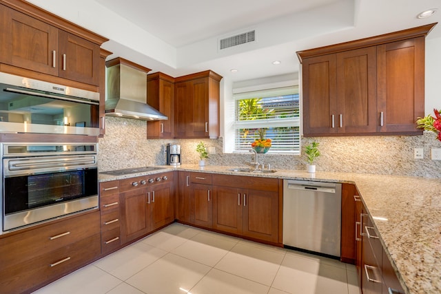 kitchen with appliances with stainless steel finishes, tasteful backsplash, light stone counters, sink, and wall chimney range hood