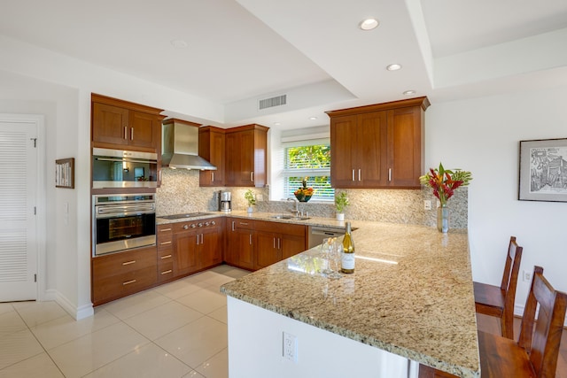 kitchen featuring kitchen peninsula, light stone counters, sink, and wall chimney exhaust hood