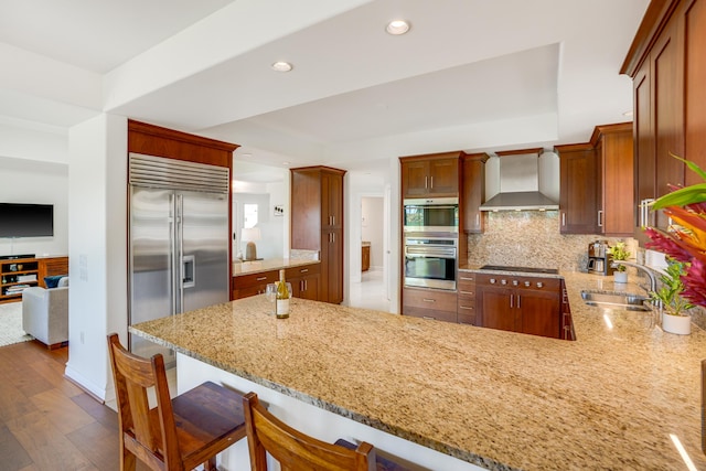 kitchen featuring kitchen peninsula, wall chimney exhaust hood, stainless steel appliances, sink, and hardwood / wood-style flooring