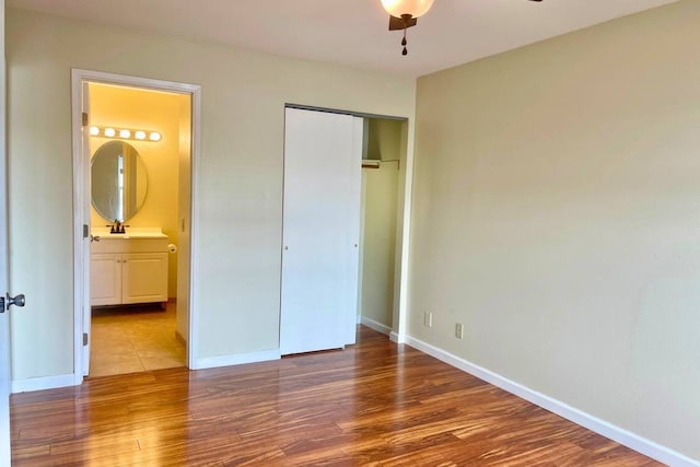 unfurnished bedroom featuring a closet, ceiling fan, connected bathroom, sink, and wood-type flooring