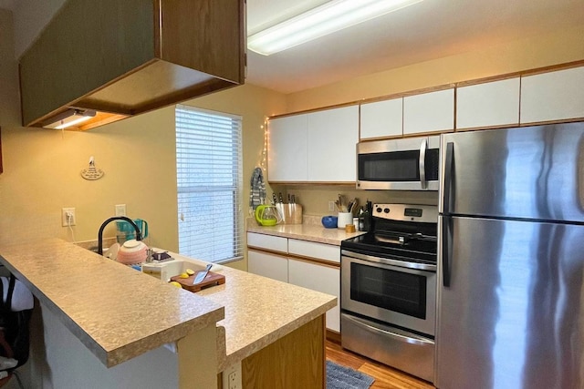 kitchen featuring appliances with stainless steel finishes, white cabinets, a kitchen bar, and light wood-type flooring