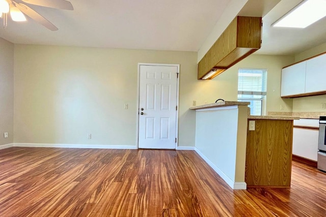 kitchen with ceiling fan, white cabinets, stove, dark hardwood / wood-style floors, and kitchen peninsula