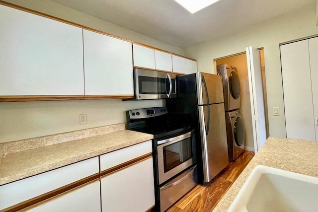 kitchen with white cabinets, sink, light wood-type flooring, stacked washer and dryer, and stainless steel appliances