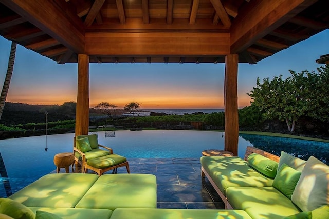 pool at dusk with a gazebo, an outdoor living space, and a water view