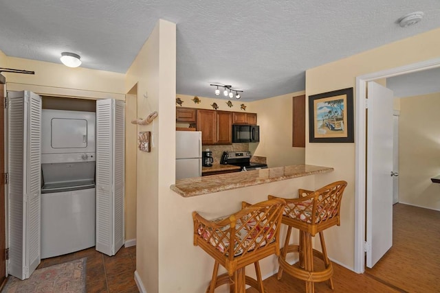 kitchen featuring white fridge, tasteful backsplash, stacked washer and clothes dryer, track lighting, and stainless steel electric range