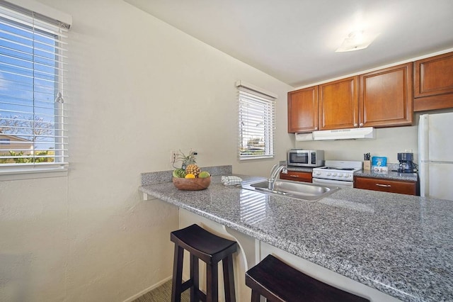 kitchen with a breakfast bar area, white stove, sink, and dark stone countertops